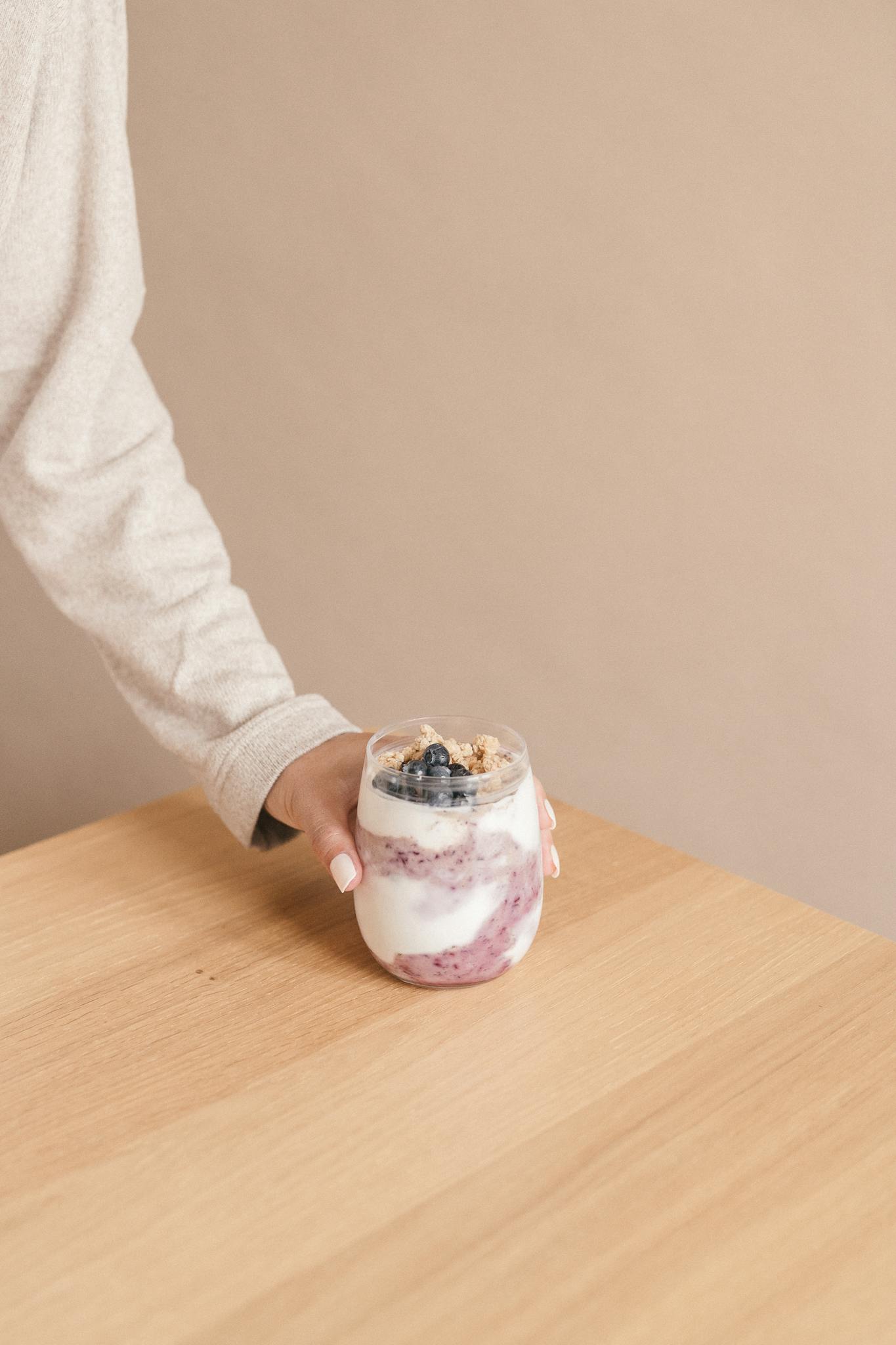 A hand holding a tasty blueberry yogurt parfait in a glass, perfect for breakfast.