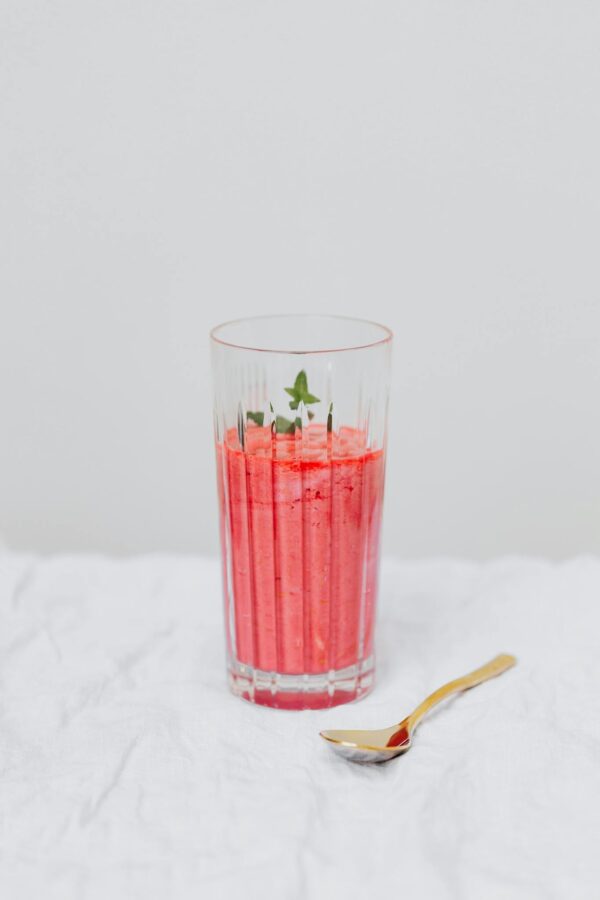 A vibrant, fresh strawberry smoothie served in a glass with a mint garnish and golden spoon.
