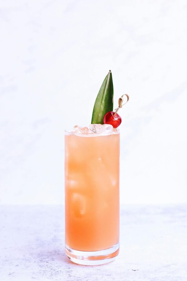 Bright and refreshing tropical cocktail with ice and cherry garnish in a tall glass.