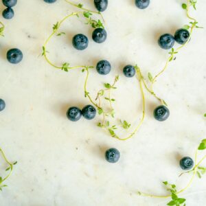 Close-up of fresh blueberries and thyme sprigs scattered on a white marble surface.