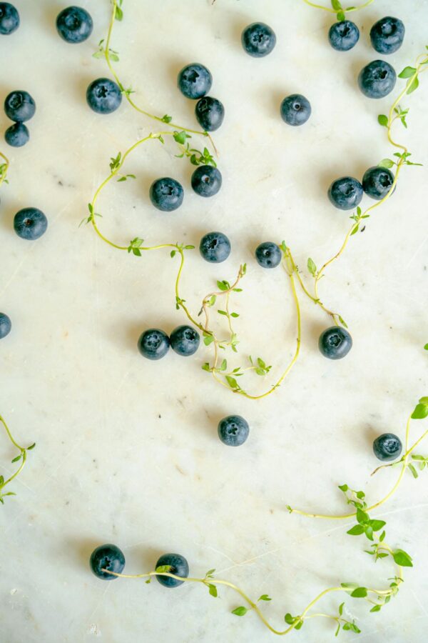 Close-up of fresh blueberries and thyme sprigs scattered on a white marble surface.
