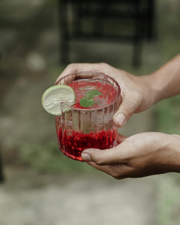 Close-up of refreshing cocktail in hand with lime and mint garnish, set outdoors in Bali.