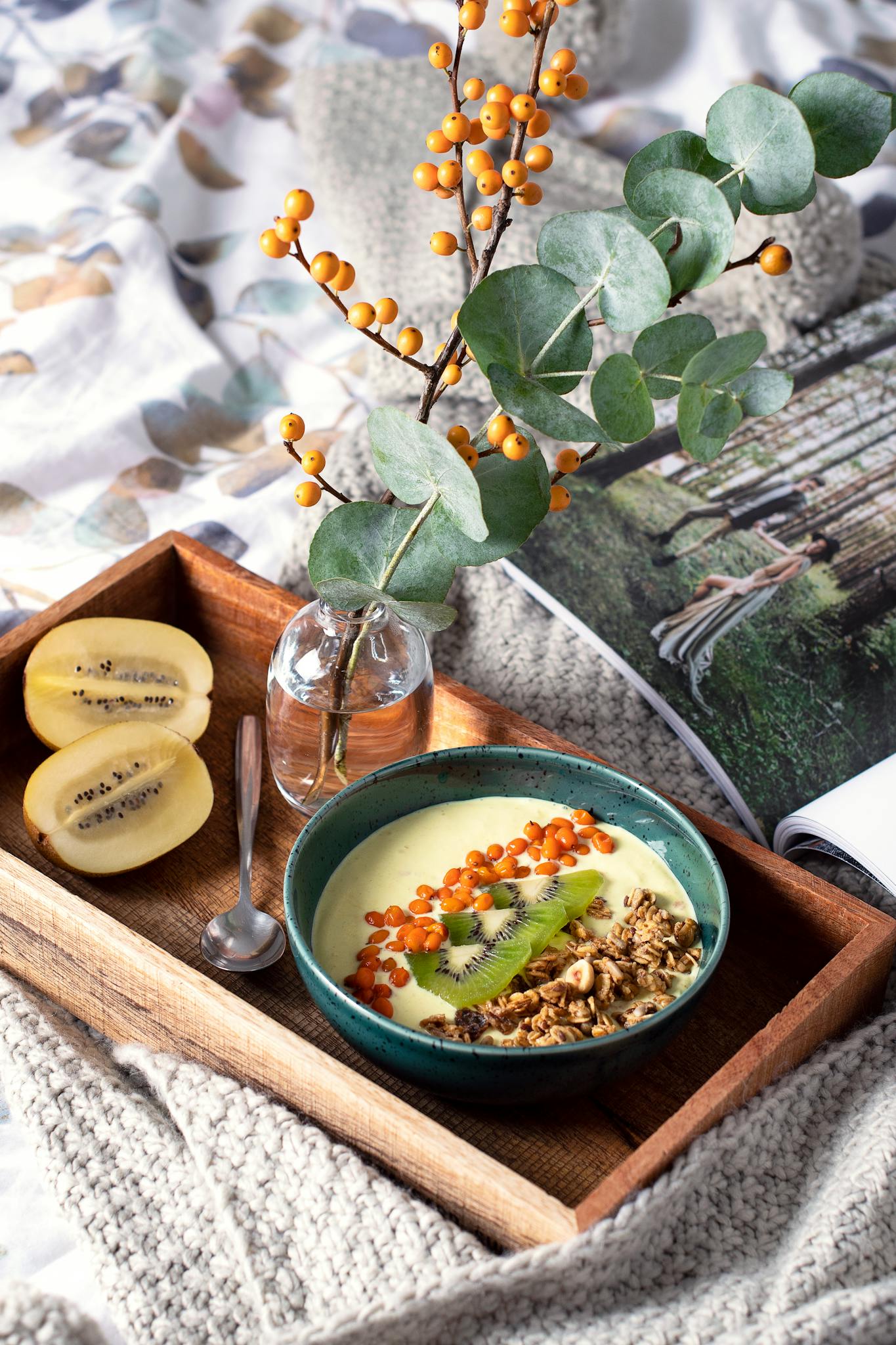 Delicious kiwi smoothie bowl with sea buckthorn, granola, and eucalyptus on a wooden tray. Perfect healthy breakfast.