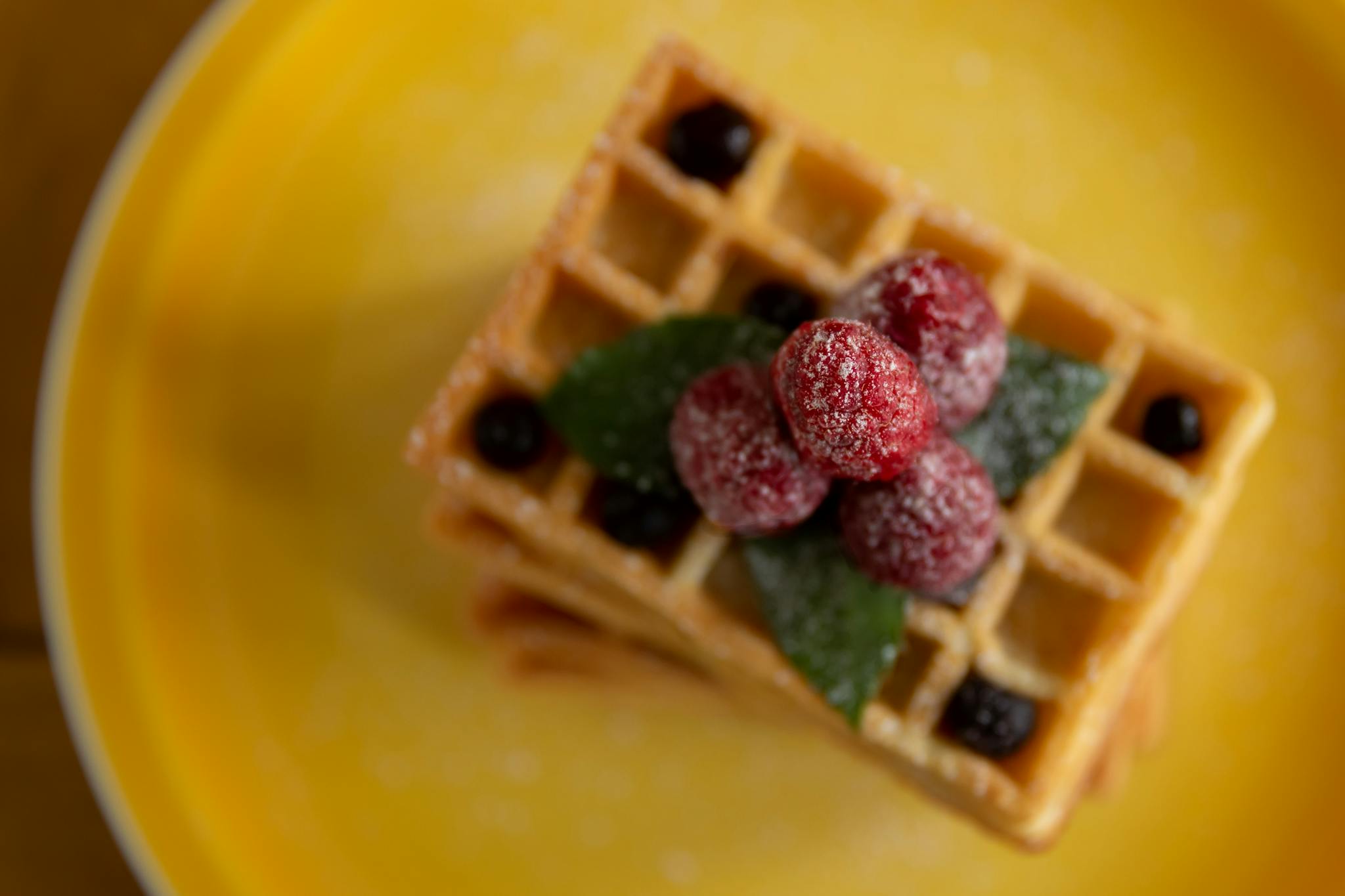Delicious waffles topped with raspberries and blueberries on a vibrant yellow plate.
