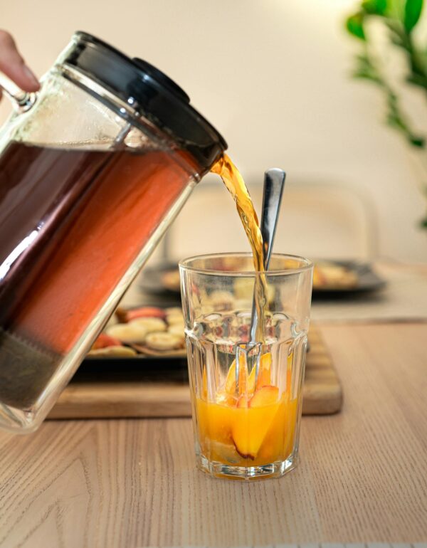 Glass of iced tea poured over fresh fruits in a cozy indoor setting.
