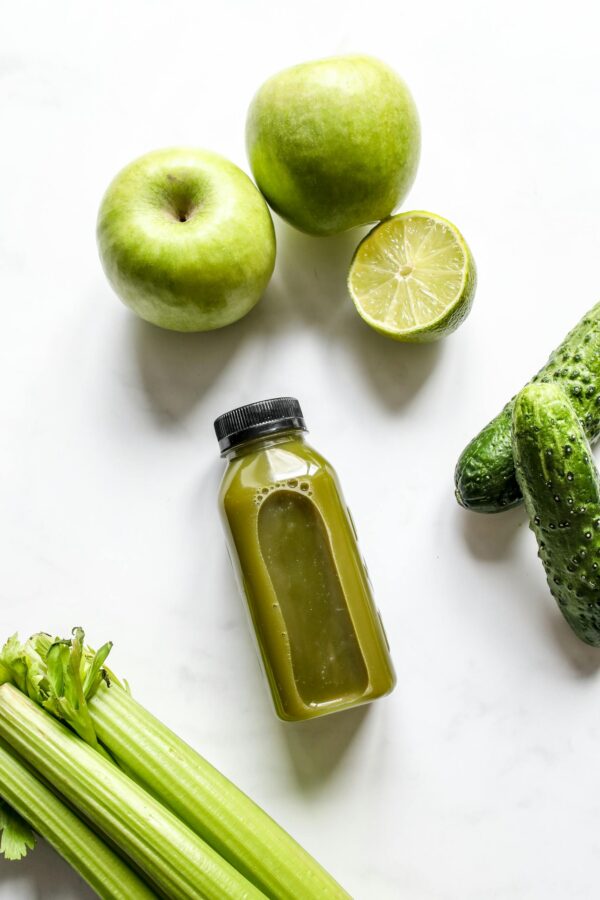 Top view of a fresh green juice surrounded by apples, celery, lime, and cucumbers.